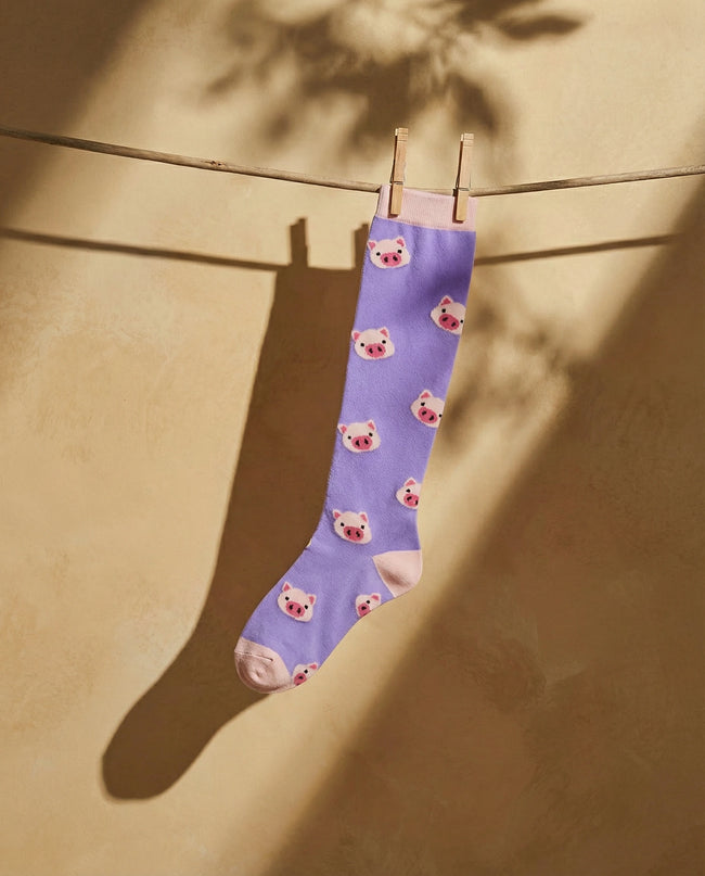 Purple sock with bear pattern hanging on a clothesline against a beige wall.