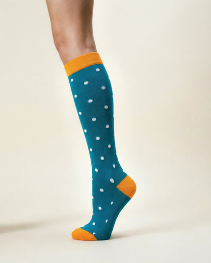 Teal knee-high sock with white polka dots and orange accents worn by a person on a beige background