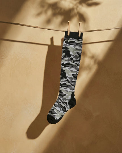 Camouflage-patterned sock hanging on a clothesline against a beige wall.