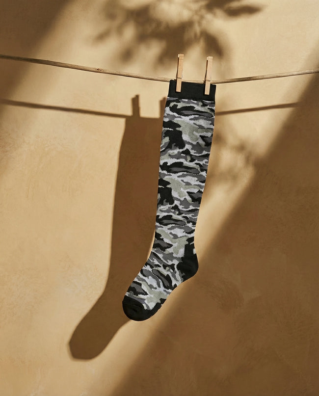 Camouflage-patterned sock hanging on a clothesline against a beige wall.