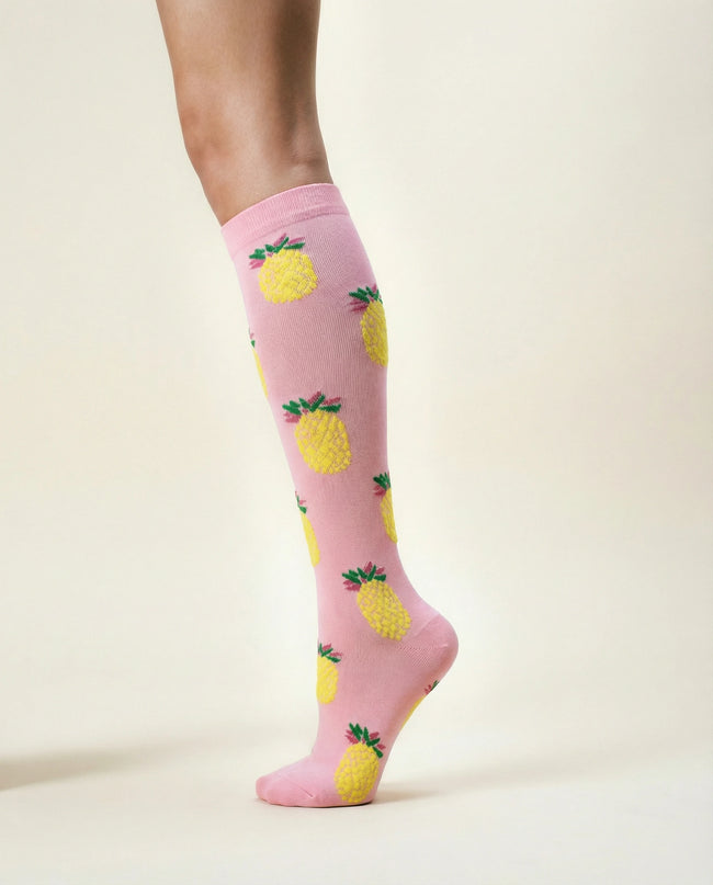 Pink knee-high socks with pineapple pattern worn by a person on a light beige background