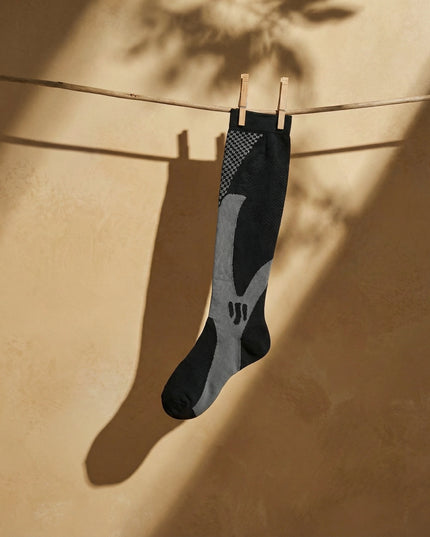 Black and gray sock hanging on a clothesline against a beige wall.