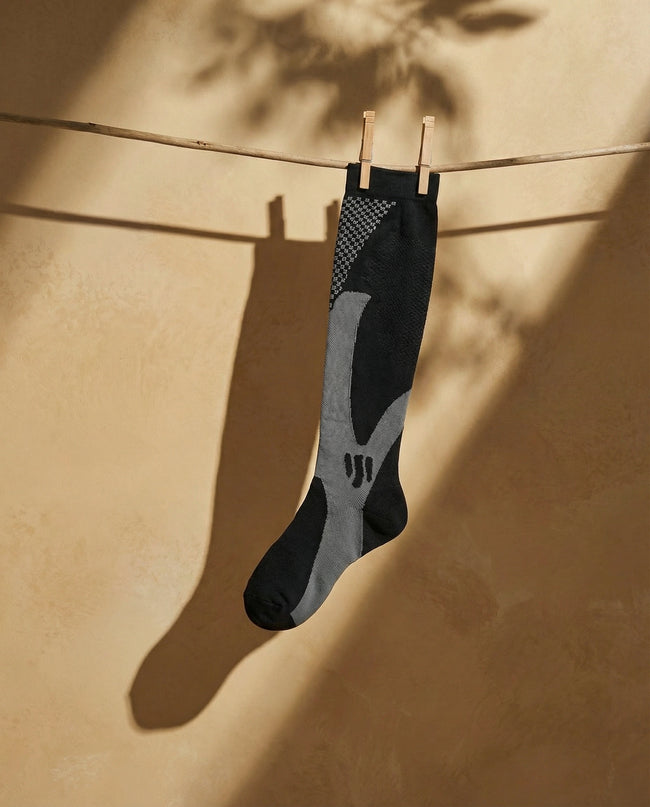 Black and gray sock hanging on a clothesline against a beige wall.