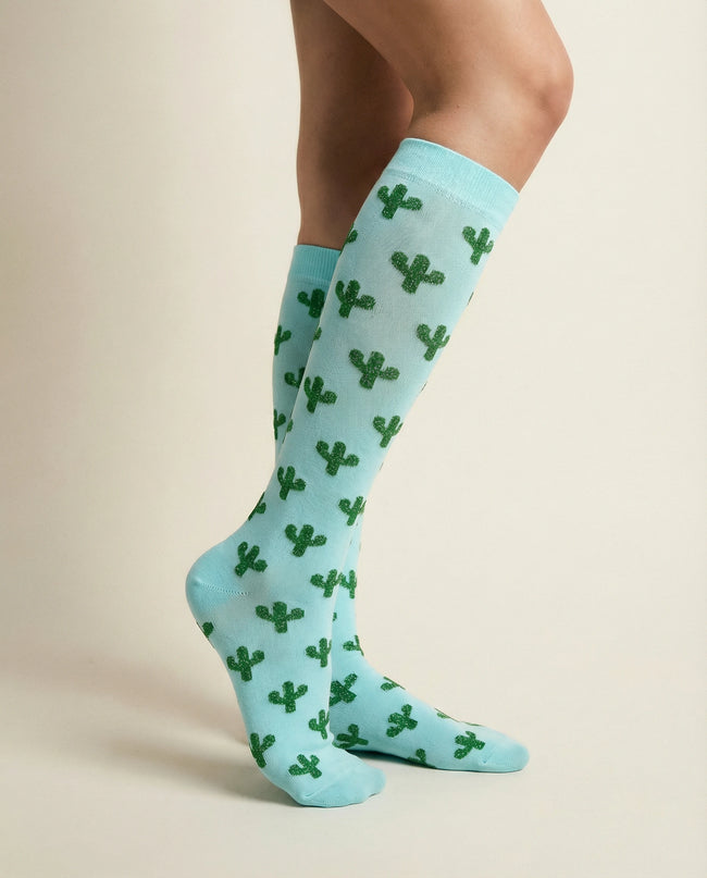 Light blue socks with green cactus patterns worn by a person on a beige background