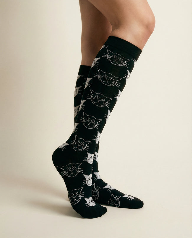 Black socks with white cat patterns worn by a person on a beige background