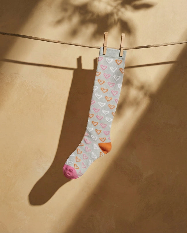 Sock with heart pattern hanging on a clothesline against a beige wall.
