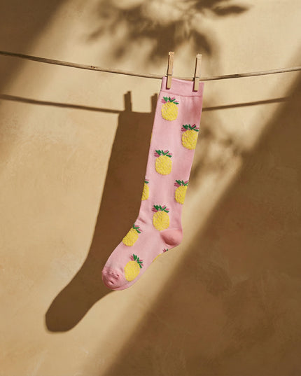 Pink socks with pineapple pattern hanging on a clothesline against a beige wall.