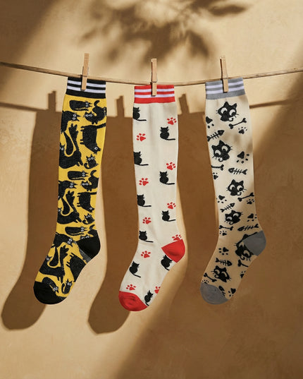 Three pairs of socks with cat patterns hanging on a line against a beige background