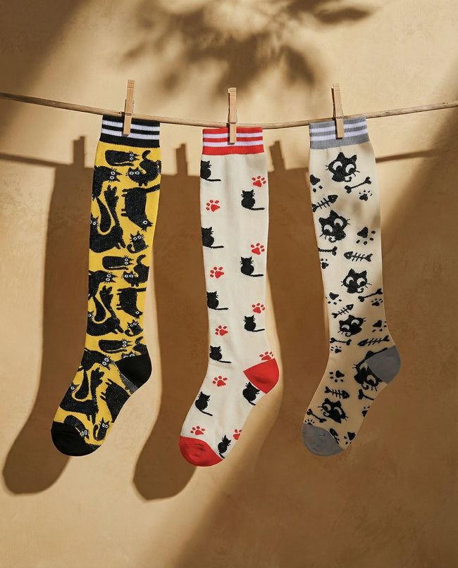 Three pairs of socks with cat patterns hanging on a line against a beige background
