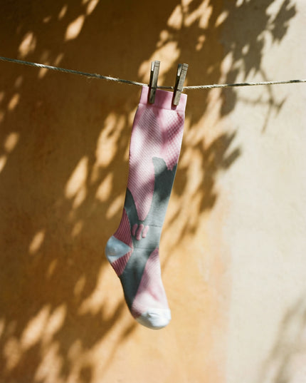 Pink and gray sock hanging on a clothesline against a yellow wall with shadow patterns.