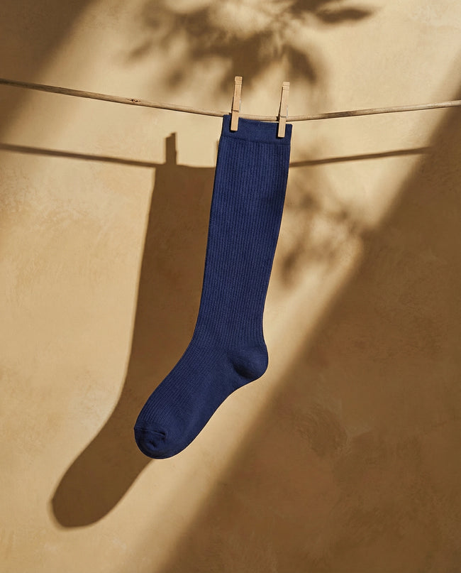 Blue sock hanging on a clothesline against a beige wall.