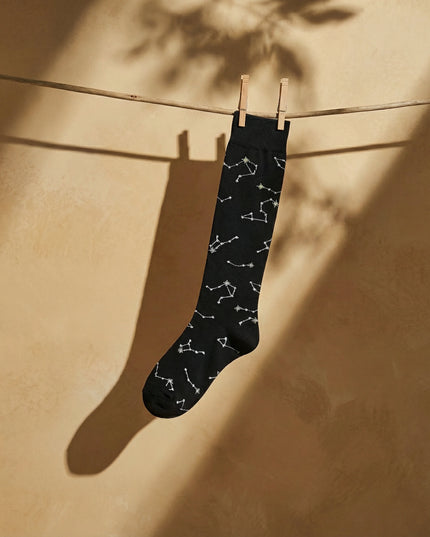 Black sock with white constellation pattern hanging on a clothesline against a beige wall.