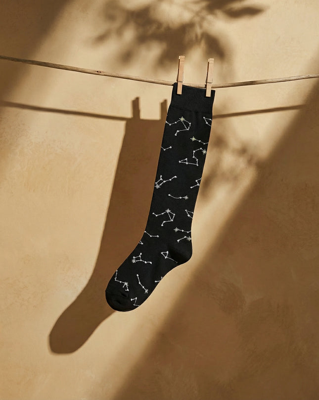 Black sock with white constellation pattern hanging on a clothesline against a beige wall.