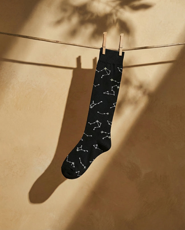 Black sock with white constellation pattern hanging on a clothesline against a beige wall.