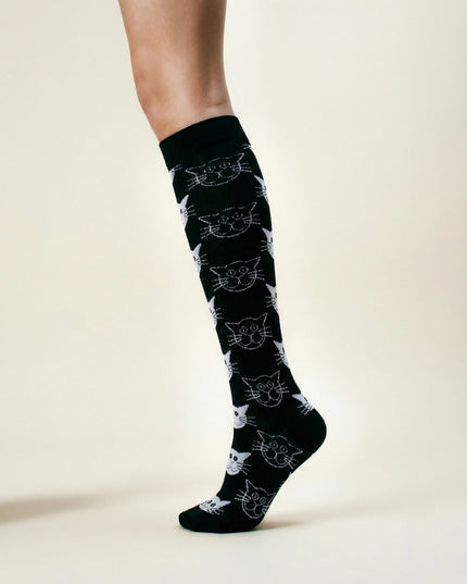 Black knee-high socks with white cat pattern worn by a person on a light background