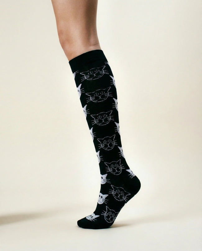 Black knee-high socks with white cat pattern worn by a person on a light background