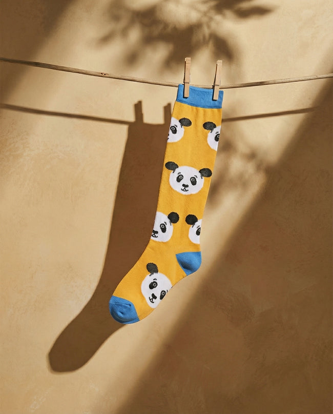 Yellow sock with panda pattern hanging on a clothesline against a beige wall.