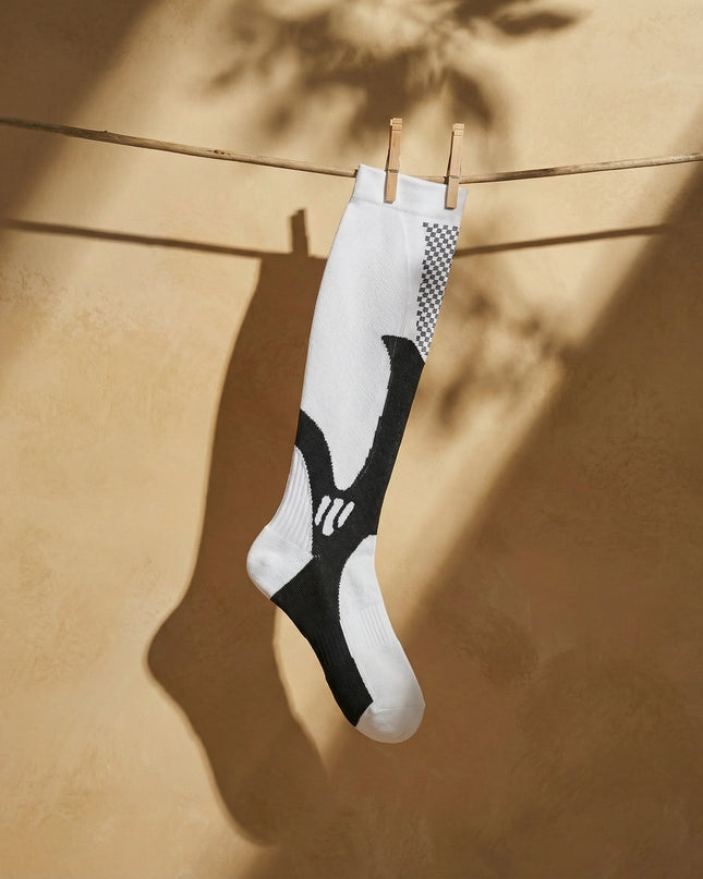 White and black sock hanging on a clothesline against a beige wall.