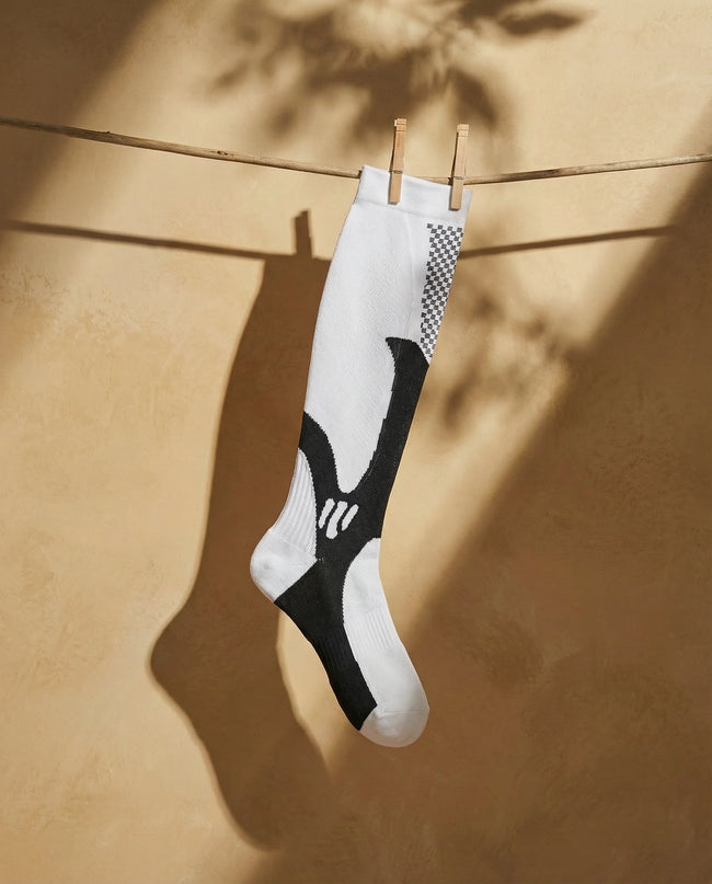 White and black sock hanging on a clothesline against a beige wall.