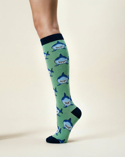 Green knee-high socks with shark pattern worn by a person on a beige background