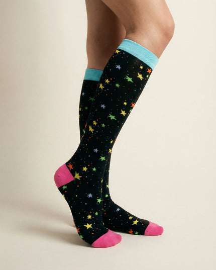 Black knee-high socks with colorful star patterns and pink toes worn by a person on a beige background