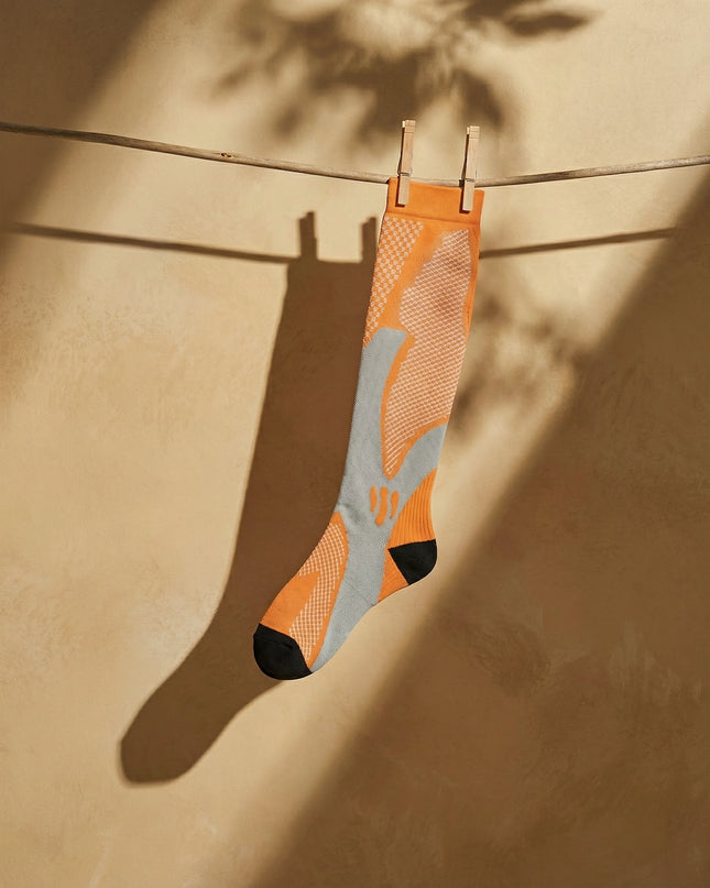 Orange and gray sock hanging on a clothesline with a beige background