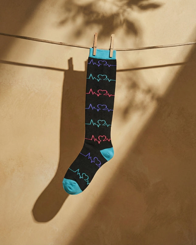 Black sock with colorful heart designs hanging on a clothesline against a beige wall.