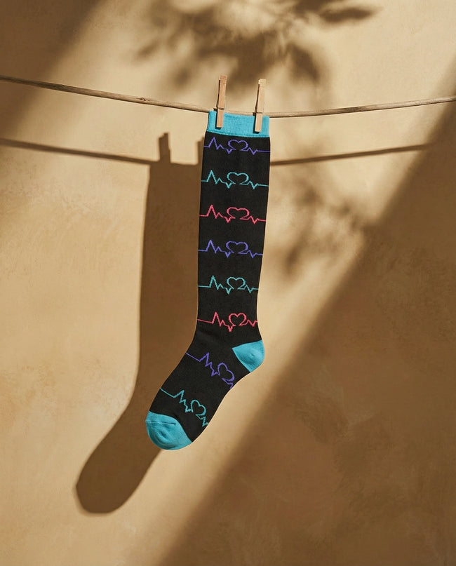 Black sock with colorful heart designs hanging on a clothesline against a beige wall.